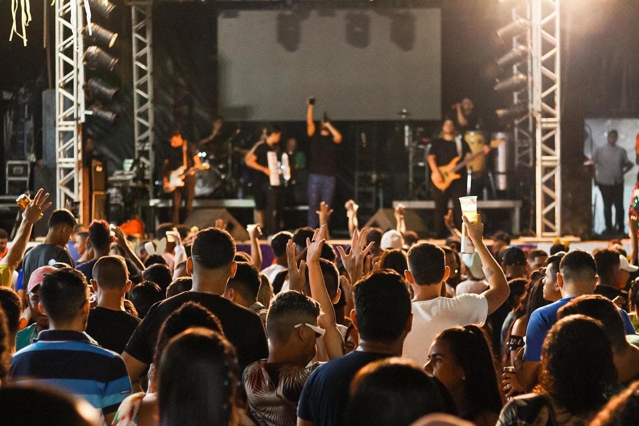 Público de costas com as mãos erguidas diante do palco durante o show